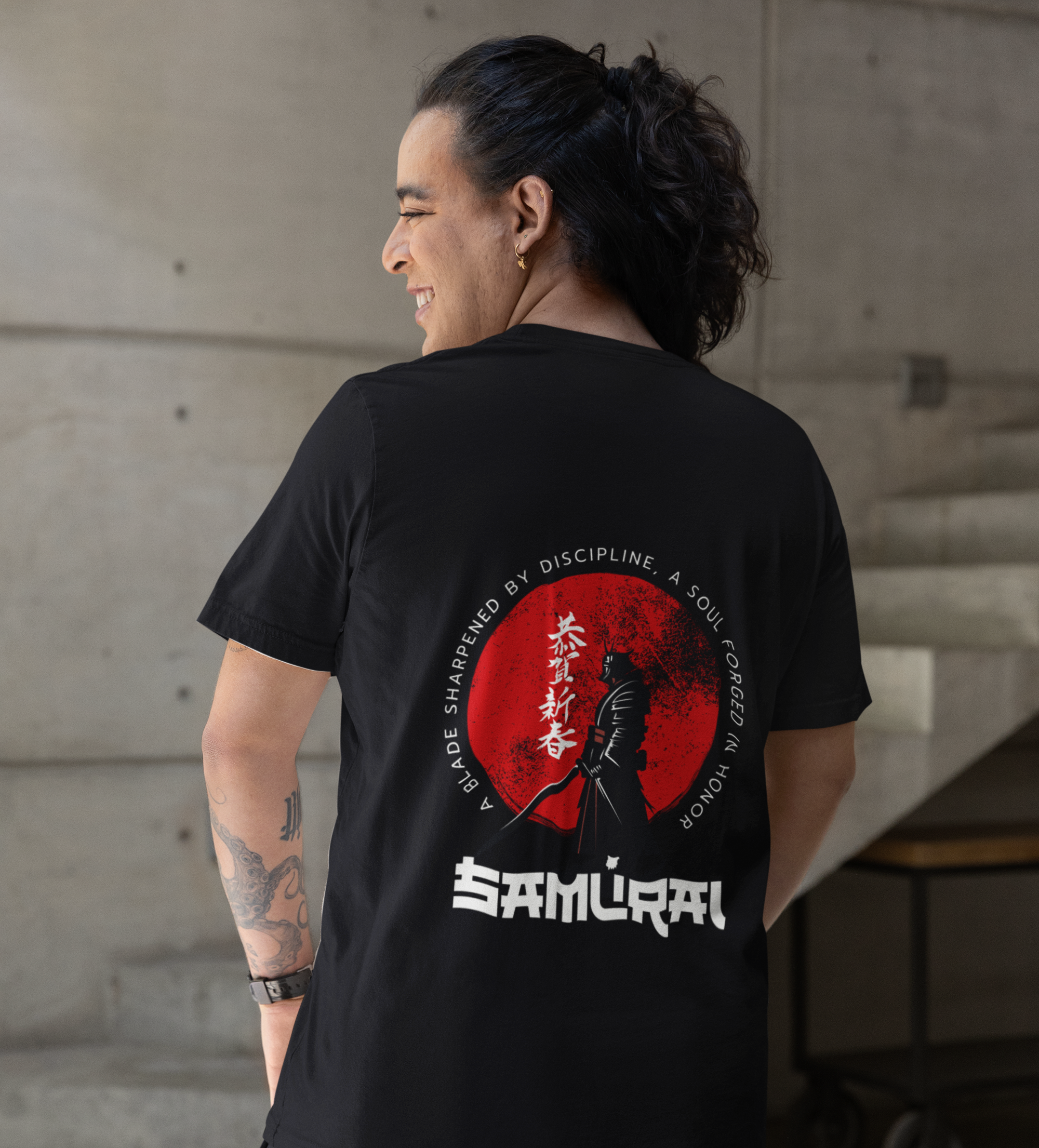 Person wearing a black t-shirt with a 'Samurai' design on the back, standing indoors.
